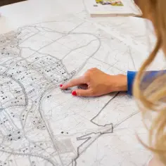 Kobieta z rudymi paznokciami wskazuje palcem na szczegółową mapę. To może być fragment geoportal miasta Rzeszowa, gdzie analizuje się plany.