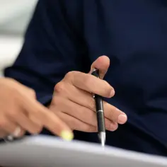 Dłonie nad dokumentami, jedna wskazuje, druga trzyma długopis. Czy notariusz sprawdza stan prawny nieruchomości?