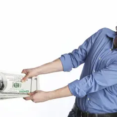 Mężczyzna z grymasem na twarzy szarpie się o stos banknotów, jakby to był trudny moment, kiedy płaci się czynsz za mieszkanie.