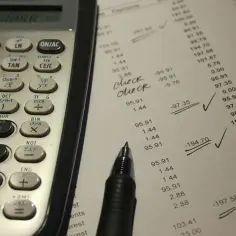 Kalkulator, długopis i dokument z liczbami i odręcznymi notatkami "check".