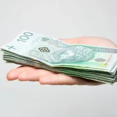 Dłoń trzyma stos banknotów 100 zł. Zastanawiasz się, jak obliczyć podatek od darowizny?