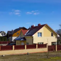 Domy jednorodzinne z czerwonymi dachami i żółtymi elewacjami, ogrodzone płotem.