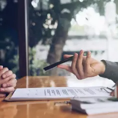 Ręka podaje długopis do podpisania umowy. Zastanawiasz się, jak sprawdzić biuro nieruchomości? Oto kluczowe kroki.