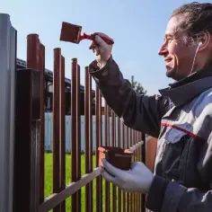 Mężczyzna maluje ogrodzenie, odnawiając je. Czy działkę rolną można ogrodzić? Tak, można ją zabezpieczyć i upiększyć.