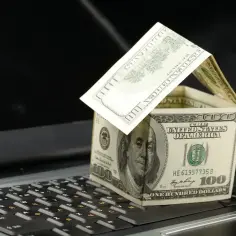 Działka budowlana zrobiona z banknotów 100 dolarów na klawiaturze laptopa. Zastanawiasz się, ile wynosi podatek za działkę budowlaną?