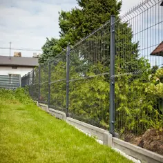 Ogrodzenie panelowe na pochyłym terenie z betonowym podmurówką i zieloną trawą.