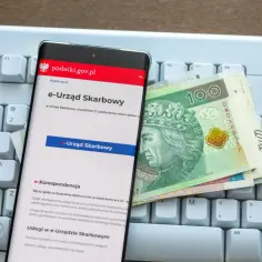 Na klawiaturze leży smartfon z aplikacją e-Urząd Skarbowy i polskie banknoty. Sprawdź, jak sprawdzić, czy podatek od nieruchomości został zapłacony.