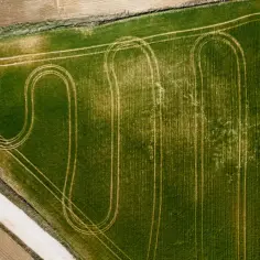 Widok z lotu ptaka na zielone pole z śladami po maszynach rolniczych. Zastanawiasz się, ile kosztuje podzielenie działki rolnej?