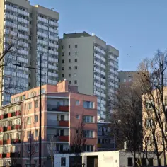 Bloki mieszkalne w słońcu. Czy spółdzielnia płaci podatek od nieruchomości? W tle wysokie budynki, na pierwszym planie różowy budynek z balkonami.