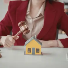 Sądowy młotek nad domkiem symbolizuje, jak sprawdzić stan prawny mieszkania.