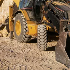 Koparka pracuje na budowie. Czy sąsiad może podnieść działkę? Maszyna z potężną łyżką i oponami gotowa do pracy.