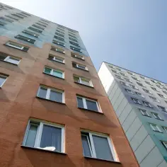 Dwa wysokie bloki mieszkalne, jeden z brązową elewacją, drugi z kolorowym wzorem. Marzysz o tym, jak dostać mieszkanie od spółdzielni?