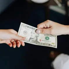 Dwie dłonie przekazujące sobie banknot 10 dolarowy.