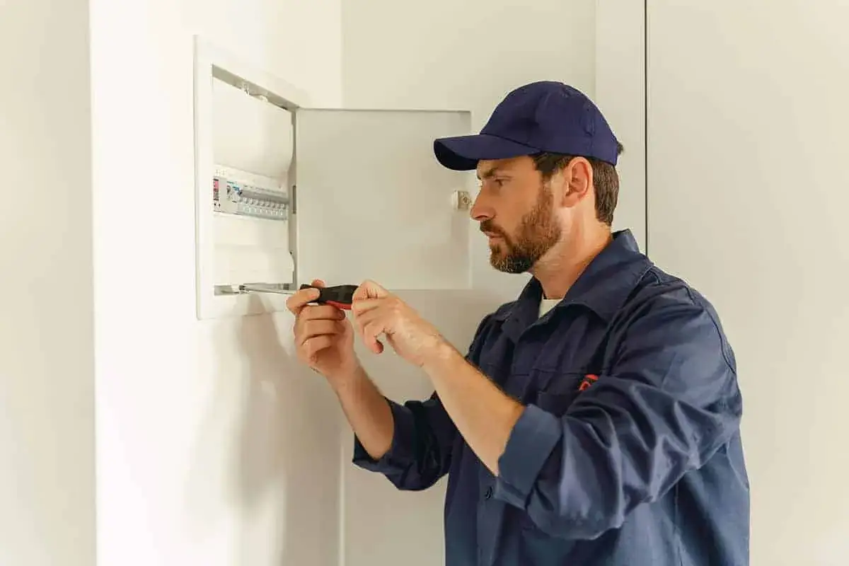 Elektryk przy skrzynce z bezpiecznikami. Dowiedz się, ile kosztuje przyłączenie prądu.