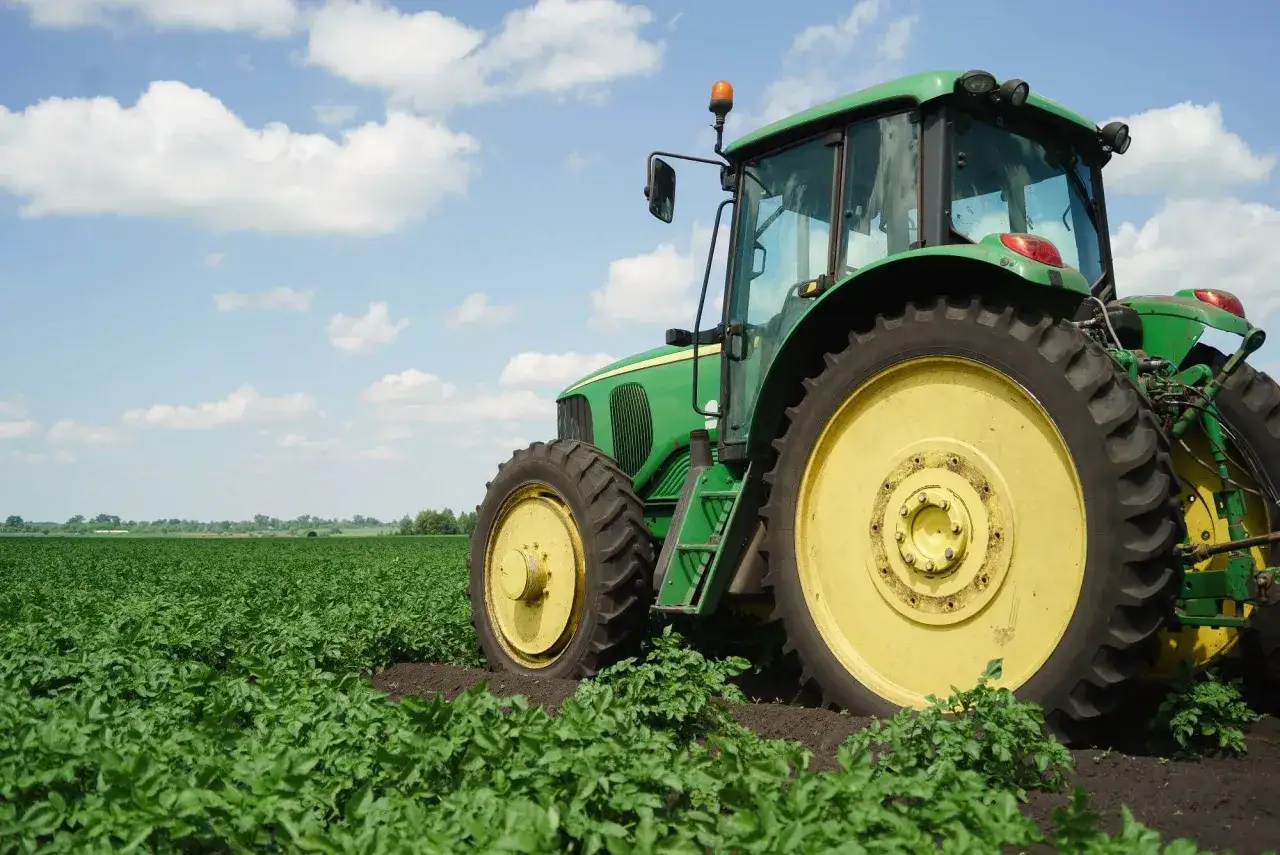 Zielony traktor na polu ziemniaków. Kto płaci podatek rolny po śmierci właściciela? Spadkobiercy przejmują obowiązki.