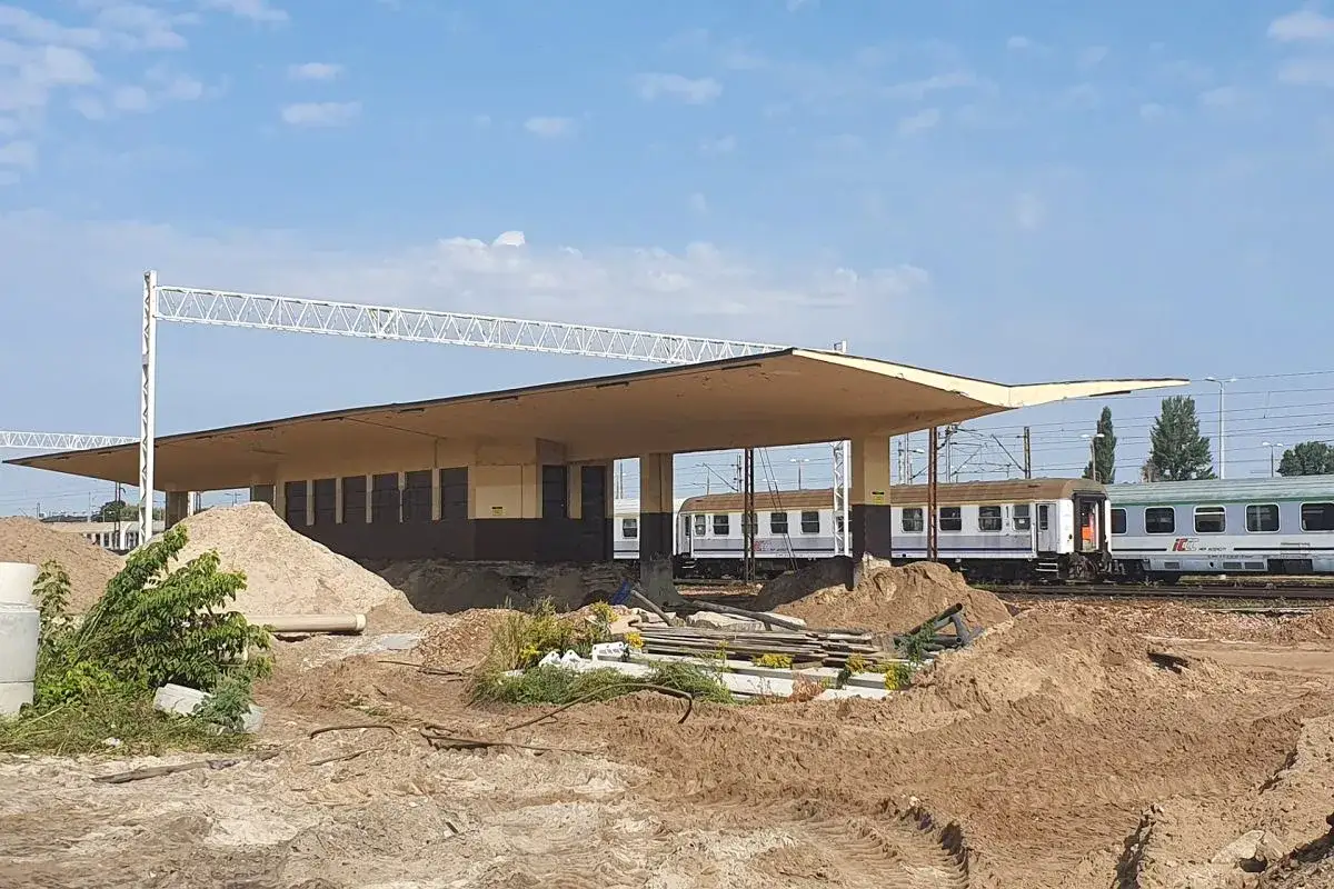 Budowa w warszawskim obszarze chronionego krajobrazu. Stary peron i pociągi na torach, otoczone placem budowy.
