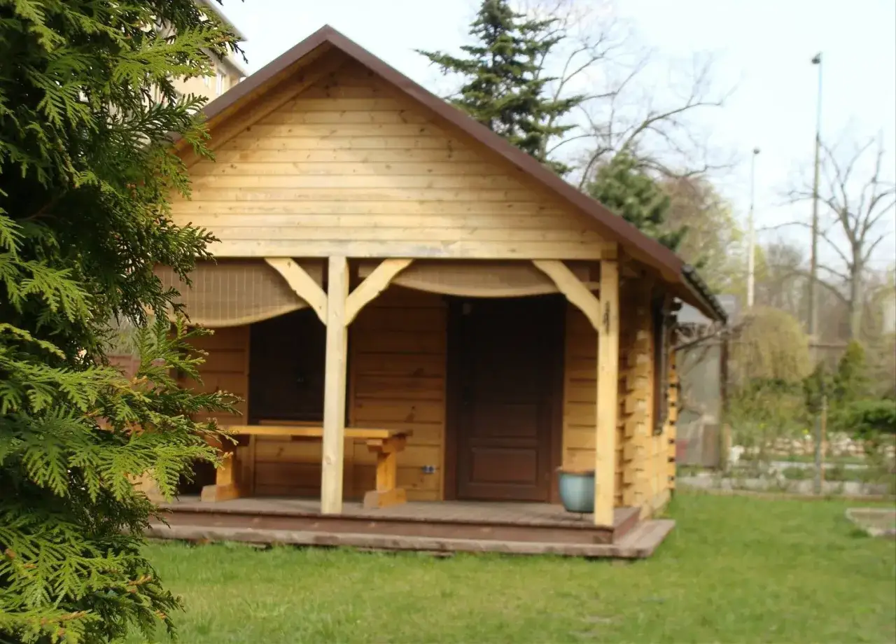 Drewniany domek na działce ROD, z werandą i ławką. Marzenie o tym, jak zamieszkać na działce ROD, staje się realne.