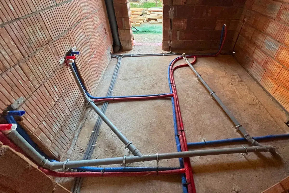 Instalacja wodno-kanalizacyjna w budowie. Rury wodne (niebieskie i czerwone) oraz kanalizacyjne (szare) ułożone na podłodze i ścianach. Sprawdź przyłącze wod kan cennik.