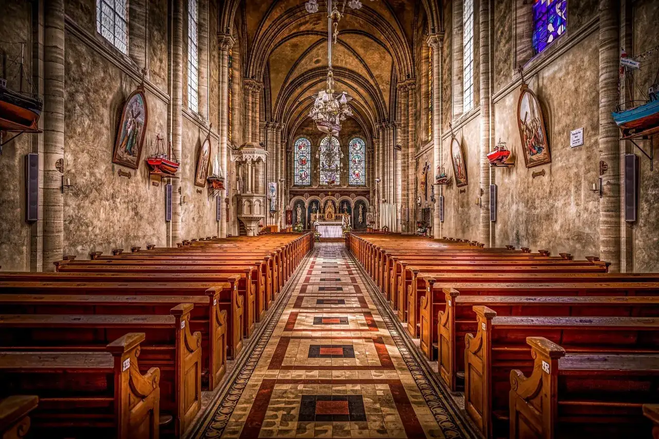 Wnętrze kościoła z rzędami drewnianych ławek i ołtarzem. Zastanawiasz się, czy kościół płaci podatek od gruntu?