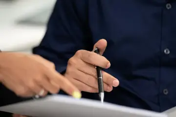 Dłonie nad dokumentami, jedna wskazuje, druga trzyma długopis. Czy notariusz sprawdza stan prawny nieruchomości?
